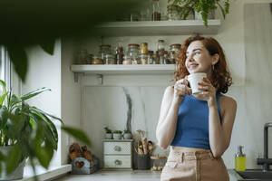 Smiling young woman standing with coffee cup at home - OSF01780