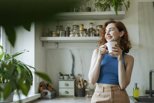 Smiling young woman standing with coffee cup at home - OSF01780