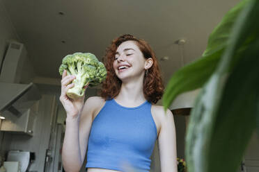 Glückliche junge Frau hält Brokkoli in der Küche zu Hause - OSF01784