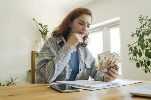 Confused young woman calculating financial bills and counting currency at home - OSF01810