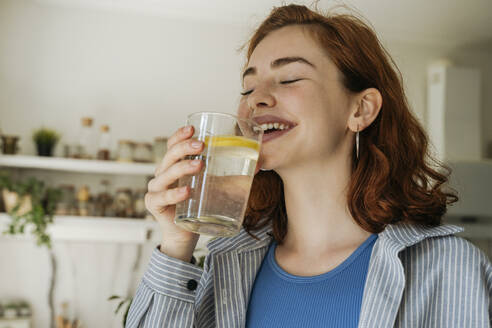 Glückliche rothaarige Frau trinkt Wasser zu Hause - OSF01818