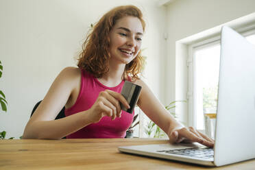 Glückliche Frau, die mit ihrer Kreditkarte am Laptop bezahlt - OSF01820