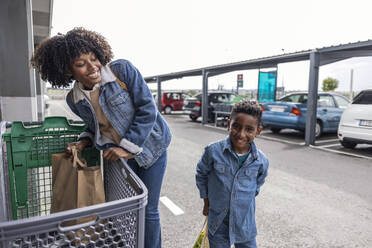 Lächelnder Junge mit Mutter, die eine Einkaufstasche im Wagen hält - JCCMF10511