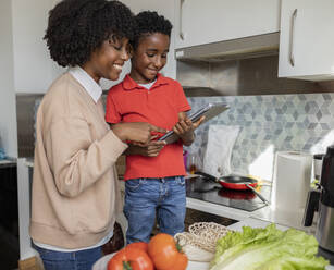 Glückliche Mutter und Sohn verwenden einen Tablet-PC in der Küche zu Hause - JCCMF10525