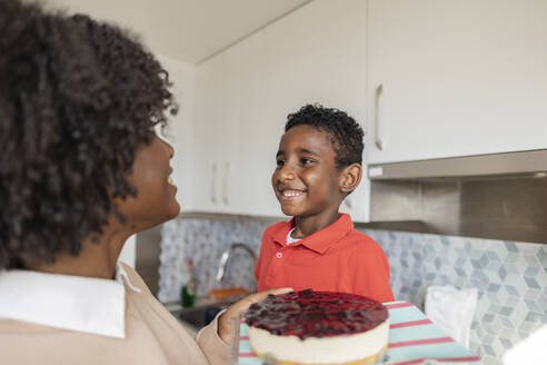 Glückliche Mutter und Sohn mit Kuchen in der Küche zu Hause - JCCMF10529