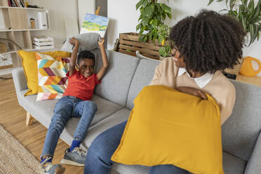 Happy boy playing pillow fight with mother on sofa at home - JCCMF10533