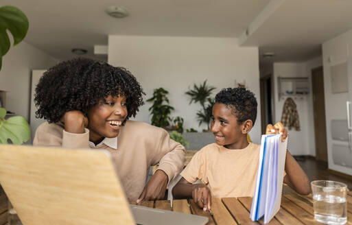 Happy son showing homework to mother at home - JCCMF10552