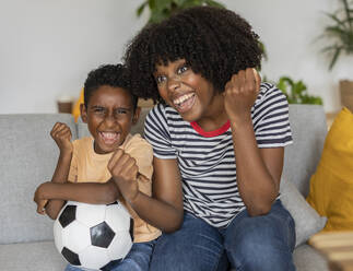 Happy mother and son cheering and sitting on sofa at home - JCCMF10574