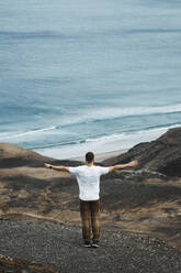 Man with arms outstretched standing on volcanic landscape in front of sea at Fuerteventura - RSGF00943
