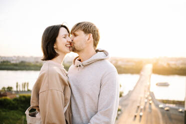 Happy man kissing woman on sunny day at riverbank - ANAF01598