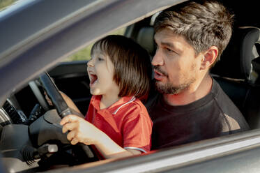 Fröhlicher Junge hält das Lenkrad, während sein Vater im Auto sitzt - ANAF01617