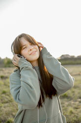 Happy teenage girl listening to music with headphones at field - ANAF01618