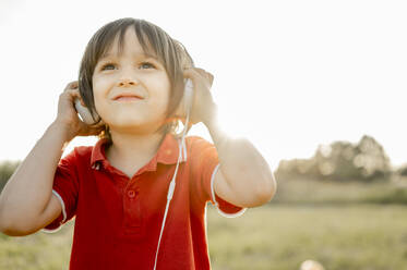 Smiling boy wearing headphones listening to music on sunny day - ANAF01620
