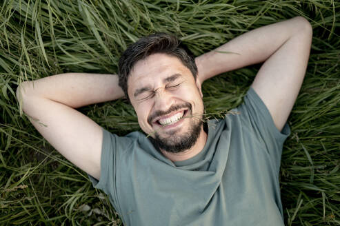 Happy man with beard lying on grass in field - ANAF01624