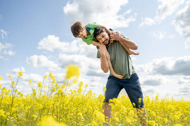 Fröhlicher Vater und Sohn, die sich an einem sonnigen Tag auf einem Feld vergnügen - ANAF01626