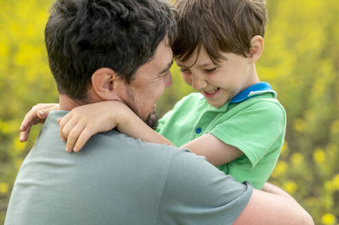 Glücklicher Vater, der seinen Sohn auf dem Feld umarmt - ANAF01630