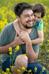 Glücklicher Sohn umarmt Vater auf gelbem Blumenfeld - ANAF01632