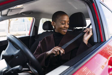 Smiling woman adjusting seat belt in car - PNAF05481