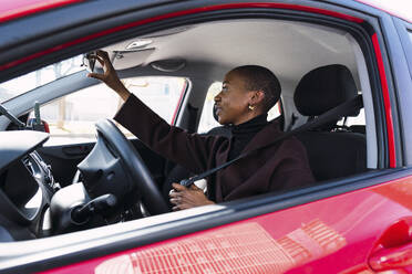 Woman adjusting rear-view mirror in car - PNAF05483