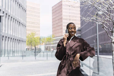 Lächelnde Geschäftsfrau, die im Büropark mit ihrem Smartphone telefoniert - PNAF05540