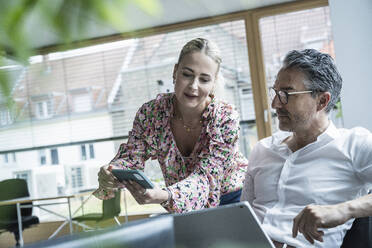 Businesswoman showing smart phone to businessman discussing in office - UUF29197