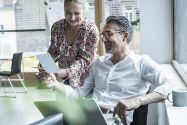 Smiling businesswoman and businessman looking at photograph in office - UUF29200