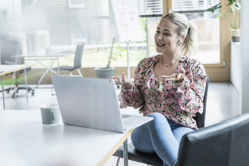 Selbstbewusste Geschäftsfrau, die über einen Laptop im Büro sitzend einen Videoanruf führt - UUF29202