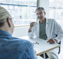 Doctor advising patient sitting at table in clinic - UUF29227