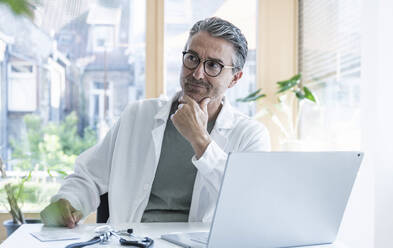 Nachdenklicher Arzt am Schreibtisch mit Laptop in einer Klinik - UUF29230