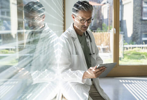 Arzt mit Tablet-PC vor einem Fenster in einer Klinik - UUF29233
