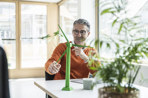 Businessman turning wind turbine model on table in office - UUF29251