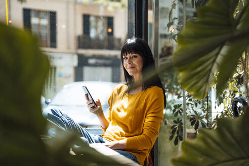 Lächelnde reife Frau sitzend mit Smart Phone - JOSEF19723