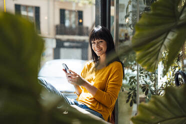 Glückliche Frau mit Smartphone in einem Café sitzend - JOSEF19725