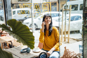 Lächelnde reife Frau, die in einem Café mit einem Smartphone telefoniert - JOSEF19728