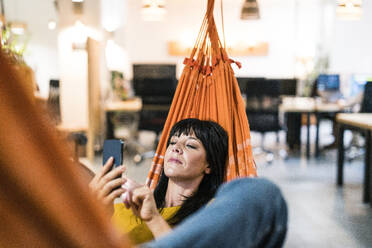 Businesswoman relaxing and using smart phone in office - JOSEF19736