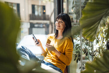 Happy woman with credit card and mobile phone sitting in cafe - JOSEF19740