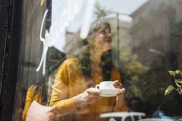 Glückliche reife Frau mit Kaffeetasse im Café sitzend durch Glas gesehen - JOSEF19748