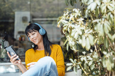 Happy woman wearing wireless headphones listening to music and using mobile pone - JOSEF19777