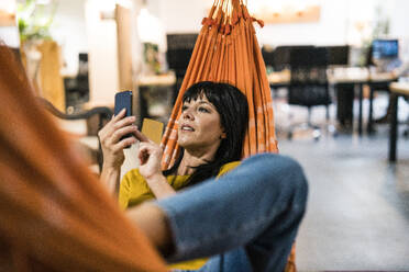 Businesswoman using smart phone in hammock - JOSEF19794