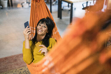 Glückliche reife Geschäftsfrau entspannt mit Smartphone in der Hängematte - JOSEF19798