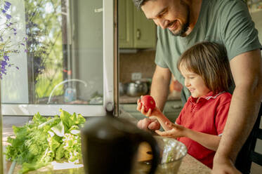 Smiling son holding tomato with father at home - ANAF01637