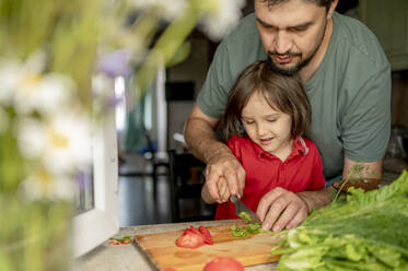 Vater bringt seinem Sohn bei, wie man zu Hause Gemüse schneidet - ANAF01643