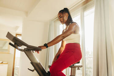 Female athlete seeking to improve her sports training has turned to a smart stationary bike for her cardio workout, using digital technology to get the most out of her home fitness routine. - JLPSF30507