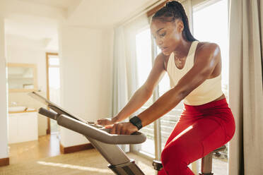 Fit and healthy African woman maintains her active lifestyle by incorporating a stationary bike into her regular exercise routine, striving to stay healthy and strong. - JLPSF30509