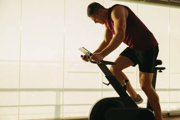 Young Caucasian man pushing himself to new limits on his state-of-the-art exercise bike, using the latest in fitness technology to achieve his health and fitness goals in the gym. - JLPSF30512