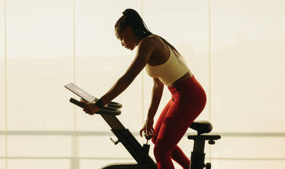 Black woman pushing herself to new heights in her fitness journey, participating in a challenging virtual cycling class. Woman crushing her fitness goals and achieving new levels of physical wellbeing. - JLPSF30518