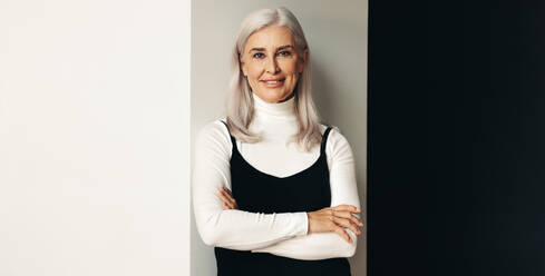 Portrait of a silver-haired senior woman looking directly at the camera with a proud and confident smile. Mature woman standing against a studio background, comfortable in her own skin. - JLPSF30536