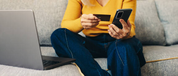 Mature woman uses her smartphone for online shopping, taking advantage of senior citizen discounts. With a content expression on her face, she enjoys the convenience of online shopping from the comfort of her own home. - JLPSF30543