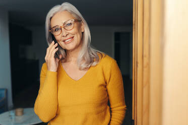 Mature woman making a phone call to communicate with her loved ones at home. With a relaxed and content expression on her face, she enjoys the ease and convenience of mobile connections. - JLPSF30544