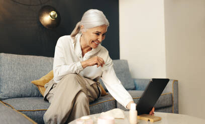 Senior woman connects with her work clients from her home office using a mobile phone. Mature female freelancer working from home, remaining productive and connected away from the office. - JLPSF30547